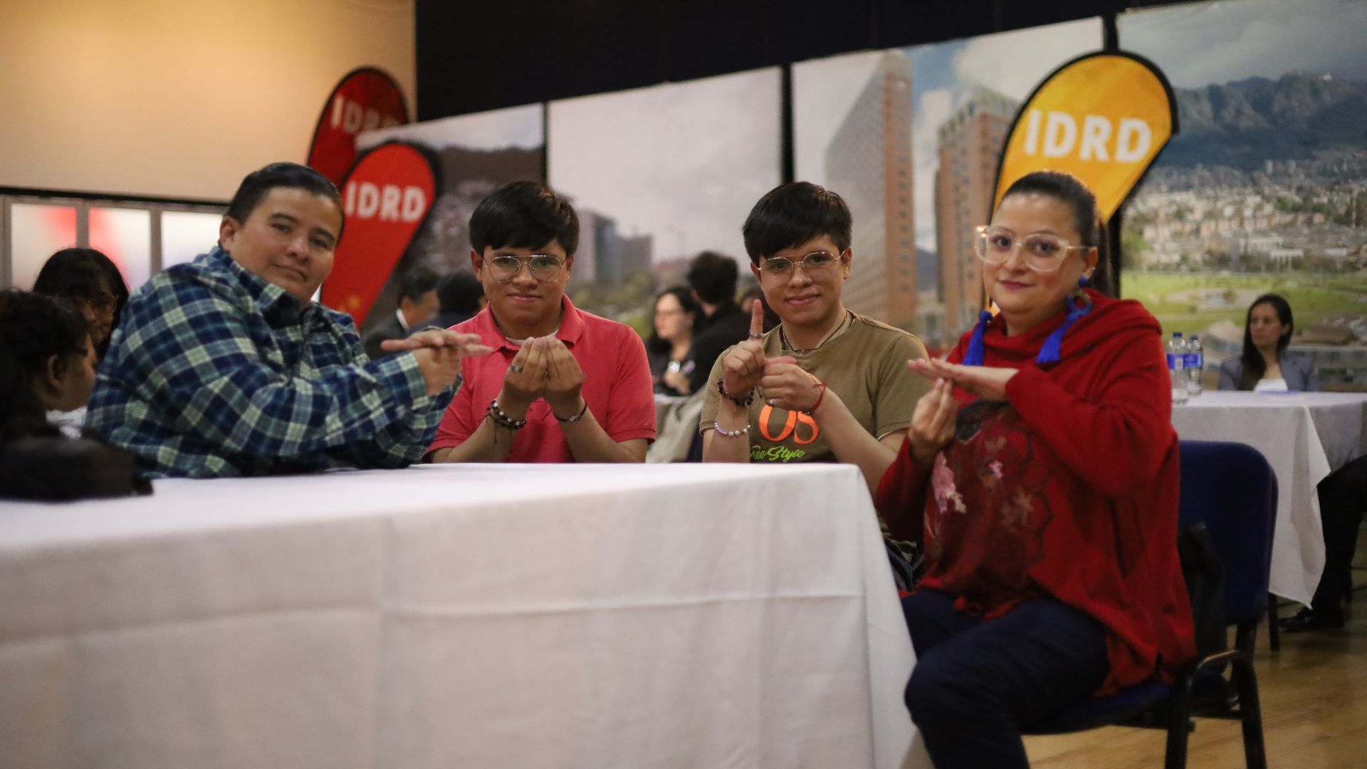 Cuatro personas mirando a cámara y haciendo una seña con las manos