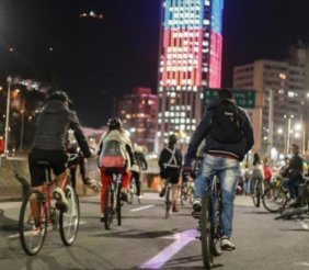 Ciclistas pedaleando por la Carrera Séptima, iluminada por la majestuosa Torre Colpatria durante la Ciclovía Nocturna.